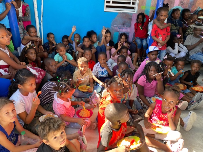 Children seated with their plates, hands raised